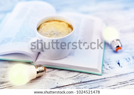 Burning light bulb, cup with coffee and book on a wooden background