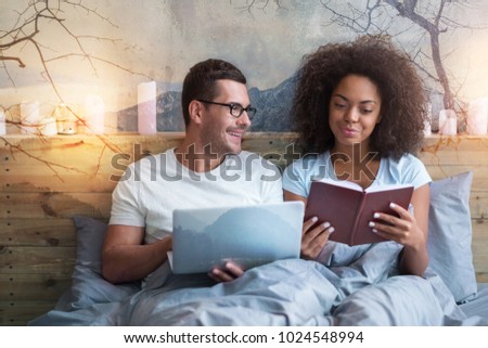 Computer device. Positive pleasant cheerful man holding a laptop and smiling while looking at his girlfriend