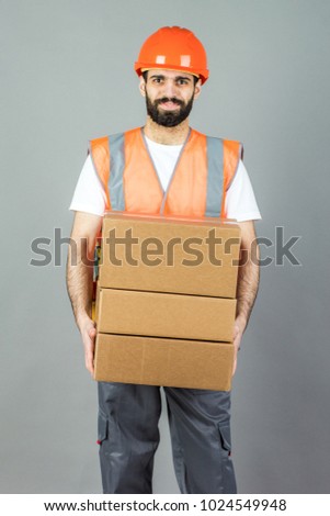 A man-builder in an orange helmet with a cardboard box in his hands. On a gray background.