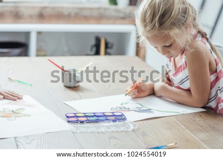 Cute blonde Caucasian girl drawing at home.