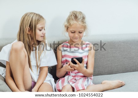Two cute Caucasian blonde smiling girls sisters using cell phone.