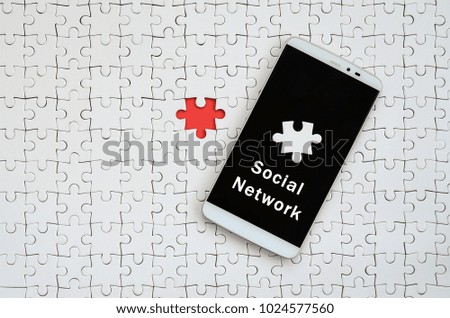 A modern big smartphone with a touch screen lies on a white jigsaw puzzle in an assembled state with inscription. Social network