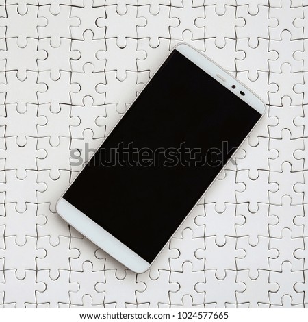 A modern big smartphone with a touch screen lies on a white jigsaw puzzle in an assembled state