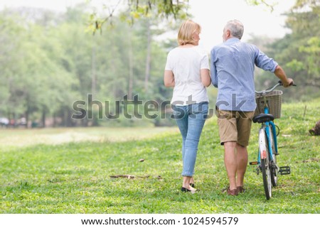 Elder healthy leisure lifestyle,Senior couple walking their bike along happy talking in the park, rear view of an older caucasian walk in a park 