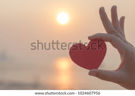 Woman hand holding red paper heart on the beach
