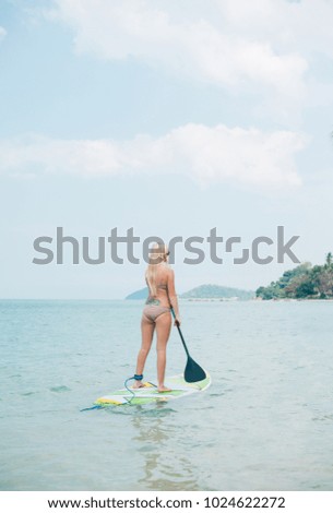 back view of woman standing up on paddleboard on sea at tropical resort