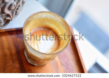 Top view of hot latte art half a glass coffee with heart foam picture served on wooden tray.