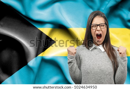 Ecstatic woman holidng fists and screaming against flag of Bahamas