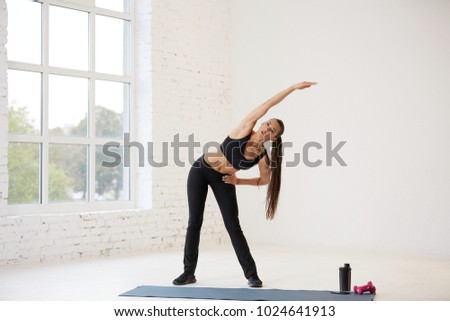 Cute young girl wearing black top and pants doing physical exercises at white background, warming up, physical activity concept, stretching exercises.