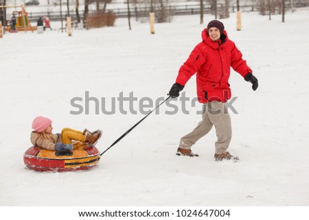 Image of father skating daughter on tubing in winter afternoon