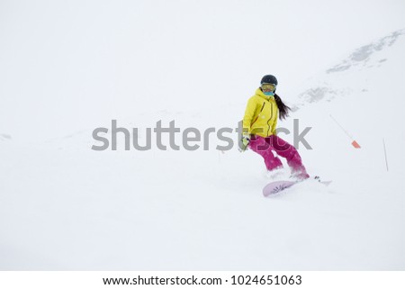 Image of athlete girl in helmet with developing hair, snowboarding from mountain slope
