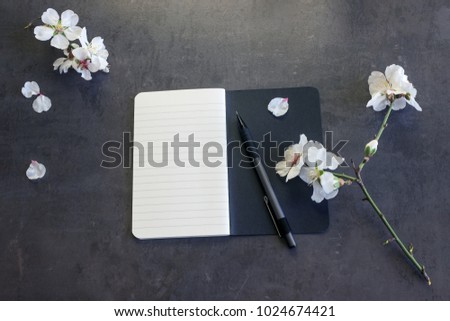  Notepad with pen and flowers of almond on a dark background. Copy space. Concept- diary keeping, creativity, business, spring mood.