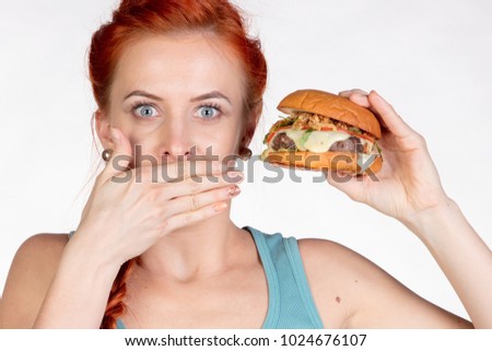 young woman covers her mouth with her hand and holds a hamburger