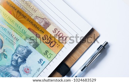 One set of Brunei money (Brunei currency) on notebook with pen, copy space