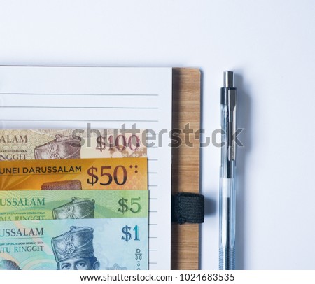 One set of Brunei money (Brunei currency) on notebook with pen, copy space