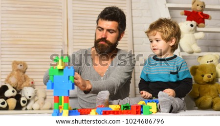 Dad and kid with toys on background build out of plastic blocks. Father and son with busy faces create colorful robot with toy bricks. Boy and bearded man play together. Family and childhood concept