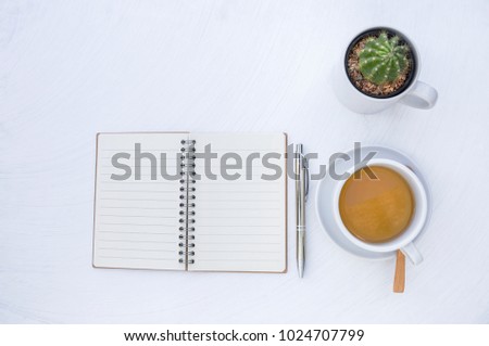Blank notebook with hot tea and cactus in white cup on white table background
