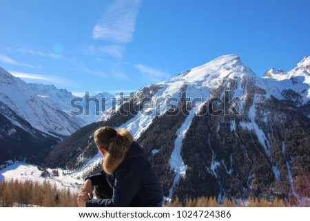 Young man in winter coat watching the snowy alpine landscape from Gimillan, Aosta Valley, Italy