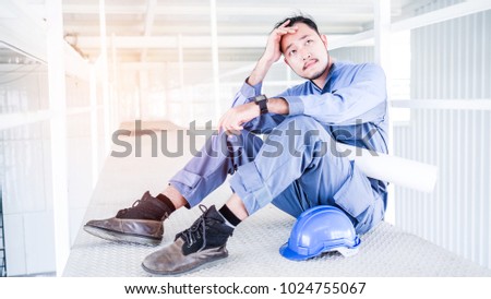 Young Asian engineers with blue helmet suffering stress fail to make mistakes in their work and business sit down on the floor at construction site. He feel very sad and serious.
