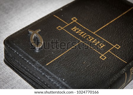 picture of a book Bible close-up in black leather binding with a zipper with a Christian pendant symbol fish on a gray background.