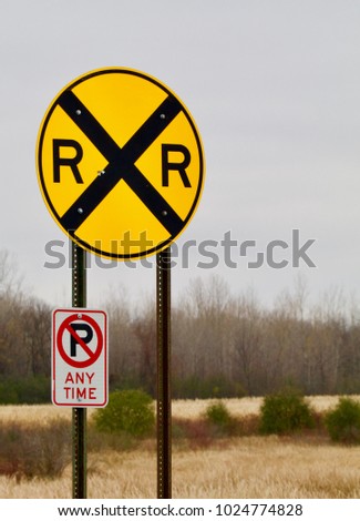 A bright yellow circular railroad crossing sign shows against a rural background.