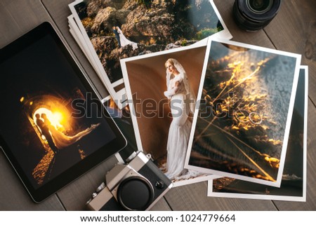 Printed wedding photos with the bride and groom, a vintage black camera and a black tablet with a picture of a wedding couple