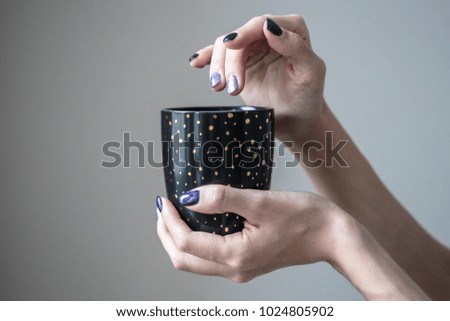 Gorgeous manicure, purple and silver nail polish, closeup photo. Female hands hold a black cup with gold dots.