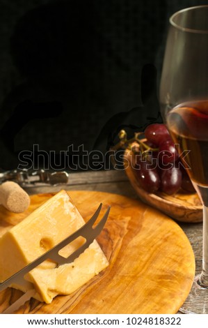 Vertical, close up, front view, glass of red wine and a wood bowl of organic grapes , wedge of french cheese, cheese knife on a round, wood serving board with bottle of wine and wine opener with cork