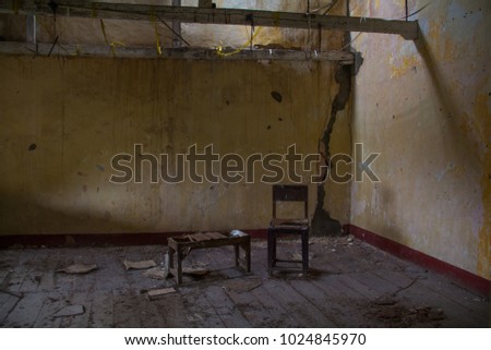 A derelict abandoned room, with water-stained peeling walls, and a broken old wood table and chair on dirty wood floorboards. Royalty-Free Stock Photo #1024845970