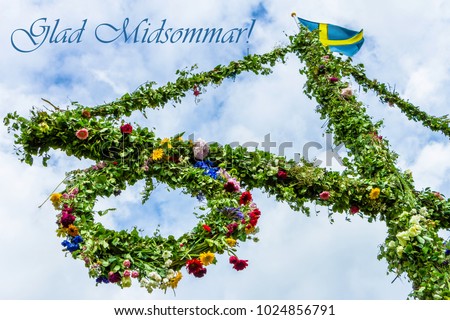 A pole and flag against blue sky and white clouds. A maypole decorated, covered in flowers and leaves. Pole after celebrating midsummer. Midsummer traditional Swedish symbol.  Kort Glad Midsommar. Royalty-Free Stock Photo #1024856791