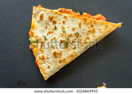 Pieces of corn tortilla with cheese and chicken in triangle on black background.