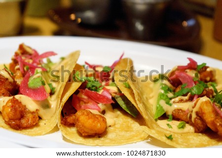 Mexican tacos of chicken with red and green chili in white sauce with avocado on a restaurant background.