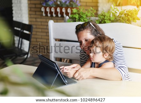 Mom and child are sitting in a cafe and watching a laptop.