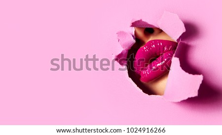 Beautiful plump bright lips of pink color peep into the slit of colored paper.Fashion, beauty, make-up, cosmetics, beauty salon, style, personal care, geometry, texture, bright, colorful, glamor, skin Royalty-Free Stock Photo #1024916266