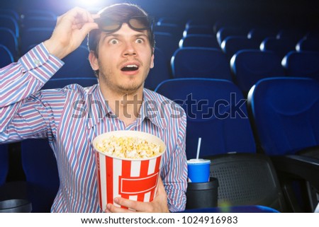 Young man looking excited taking off his 3D glasses watching a movie at the cinema technology modern entertaining leisure lifestyle weekend popcorn holidays premiere activity people.