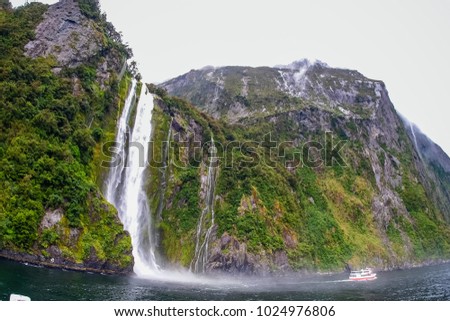 Beautiful waterfall in Milford Sounds. Tourist ferry carrying people approaching Stirling Falls, the greatest waterfalls in Milford Sound, New Zealand.