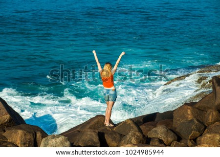 The girl stands on the beach of the ocean with her hands up