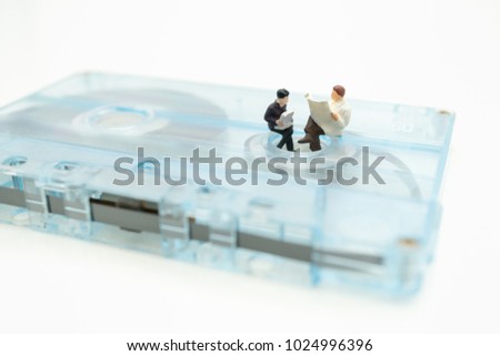 Miniature people: Business man sitting on tape cassette and reading newspaper, book with copy space using as background music learning, education, business concept.