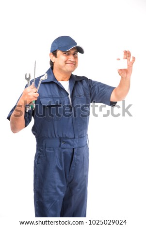 Handsome Indian Auto Mechanic presenting something or showing empty biz card while holding tools like spanner in one hand