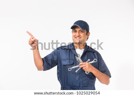 Handsome Indian Auto Mechanic presenting something or showing empty biz card while holding tools like spanner in one hand