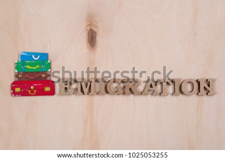 Emmigration, the word in abstract wooden letters. Background wooden surface and a pile of suitcases
