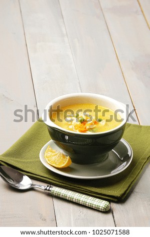 Chicken soup with vegetables in a green ceramic bowl on a green napkin and wooden table, piece of lemon and spoon on the left side, ramadan food