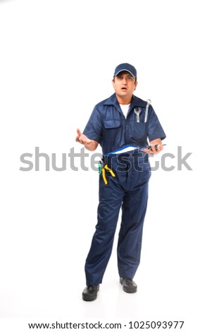 Indian happy auto mechanic in blue suit and cap holding spanner tool with laptop or check list or writing pad or using smartphone 