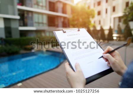 Hands of woman sign contract on background of new apartments. concept of an agreement between people, business trip. Front used with Open Font License