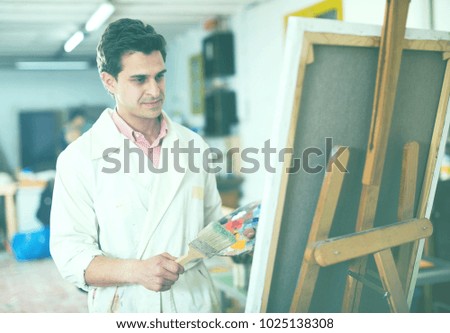 Happy art painter holding artist palette and painting on canvas