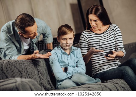 Clear explanation. Strict young parents telling their son about the drawbacks of binge-playing on the phone while the boy, scolding him, while the boy looking offended Royalty-Free Stock Photo #1025142850