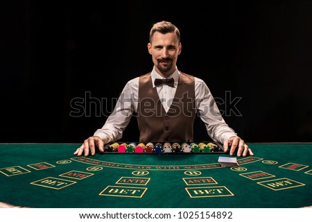 Portrait of a croupier is holding playing cards, gambling chips on table. Black background Royalty-Free Stock Photo #1025154892