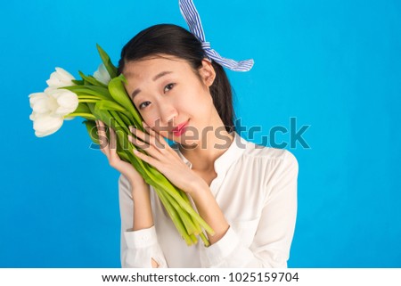 Portrait of Beautiful happy young Korean asian girl with pony tail smiling and smelling spring bouquet of white tulips or snowdrops on blue background. International Women's Day. Copy space