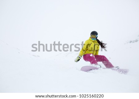 Picture of athlete girl in helmet with developing hair, snowboarding from mountain slope