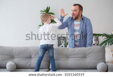 Family picture of young son standing on couch doing handshake with father